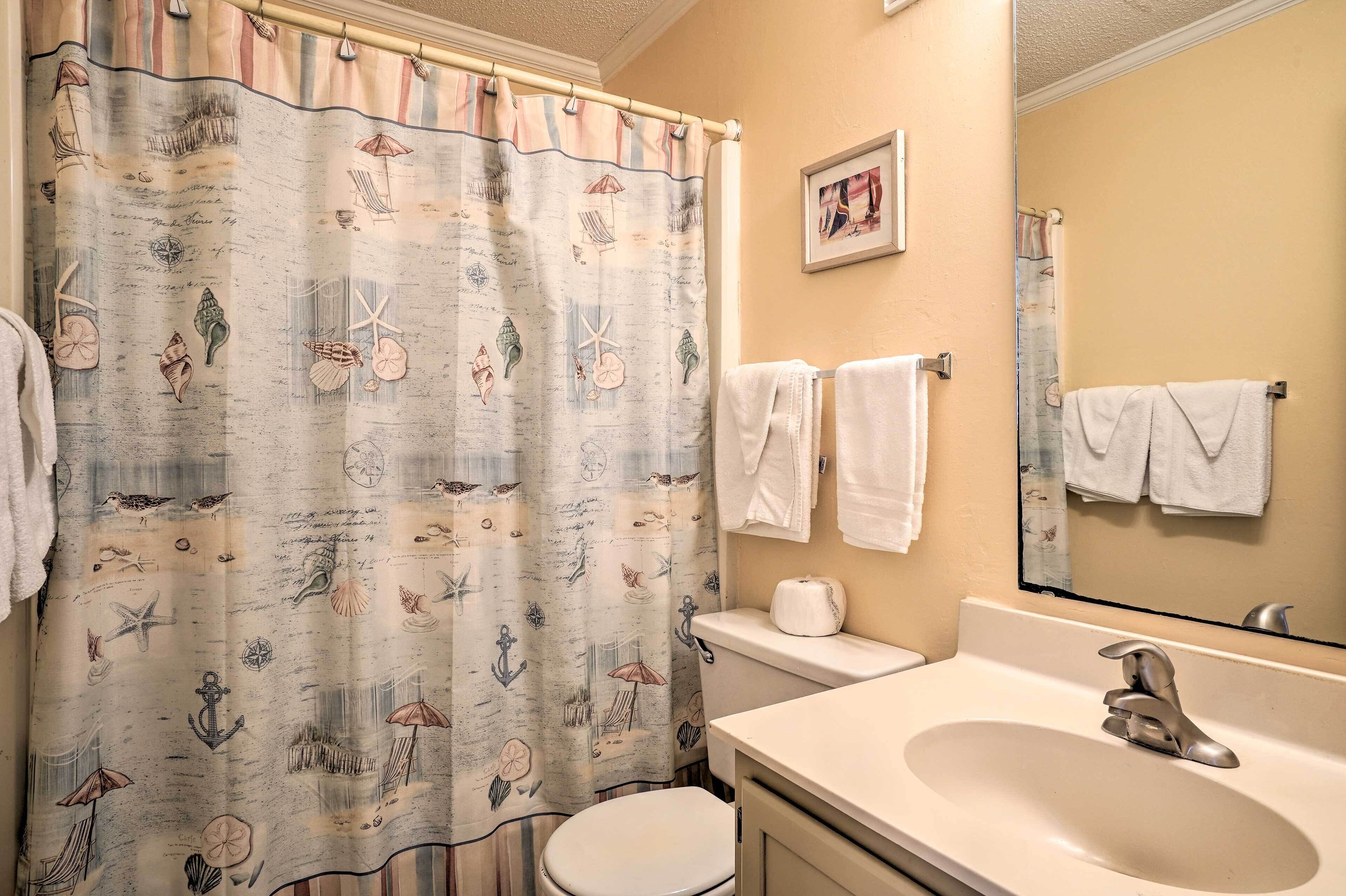 Ein Badezimmer mit einer Duschvorhang mit maritimem Dekor, einer Toilette, einem Waschbecken mit Spiegel und Handtüchern, die an der Wand hängen.