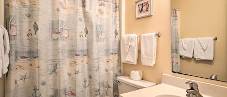 Ein Badezimmer mit einer Duschvorhang mit maritimem Dekor, einer Toilette, einem Waschbecken mit Spiegel und Handtüchern, die an der Wand hängen.