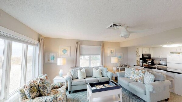 A spacious living room with two sofas, a coffee table, and a kitchen area with appliances.