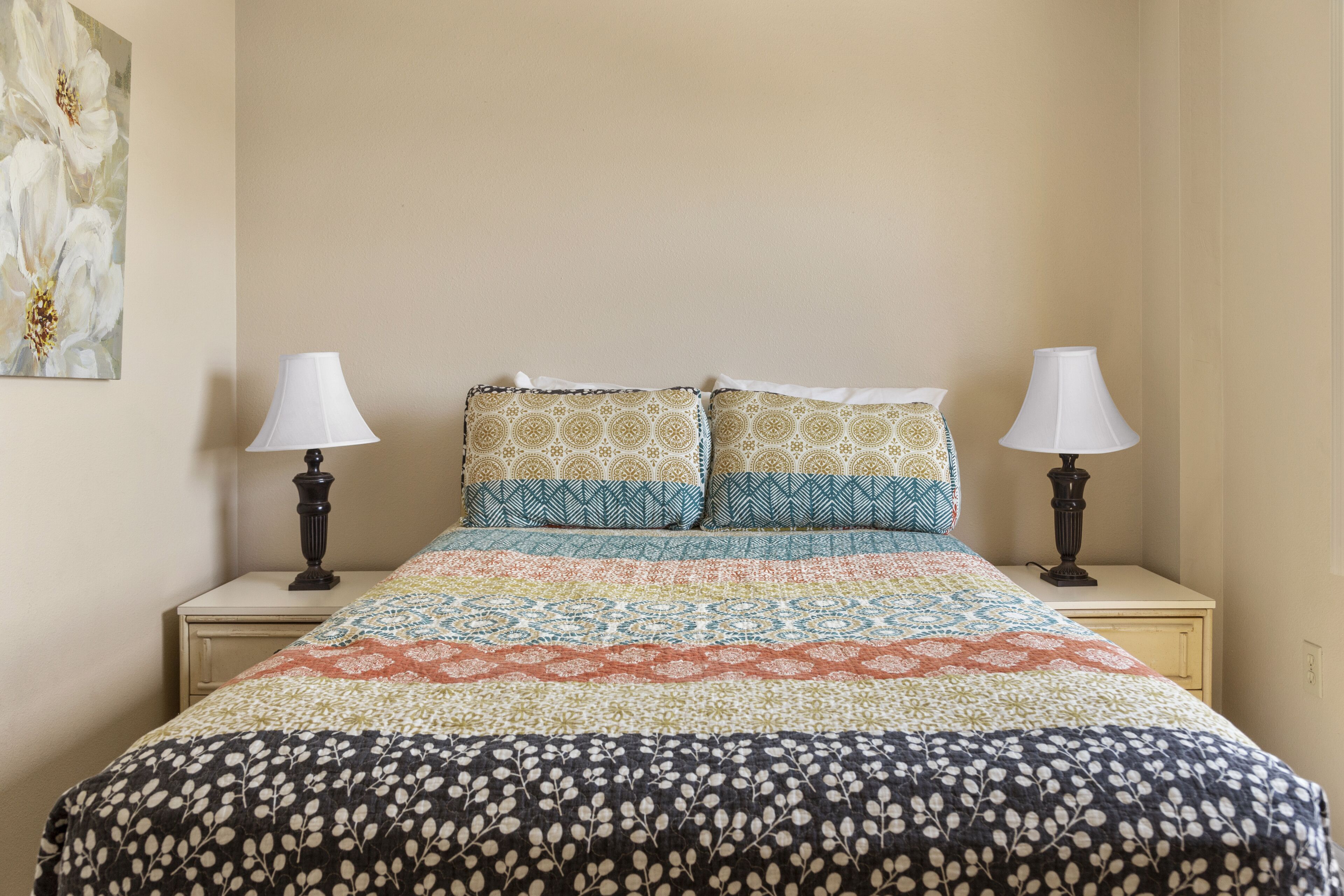 A bed with a patterned bedspread, two pillows with a geometric design, and two bedside lamps on matching nightstands.