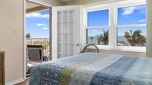 Een slaapkamer met een groot bed, een balkon met een stoel en uitzicht op de oceaan door grote ramen.