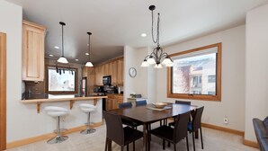 Une cuisine moderne avec des meubles en bois, un îlot central doté de tabourets, et une table à manger avec des chaises.