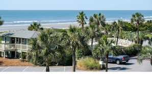 A beachfront property with a parking lot, a building with a balcony overlooking the ocean, and palm trees.