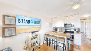 A kitchen with white cabinets, a large island, and a flat-screen TV displaying 'ISLAND REALTY'.