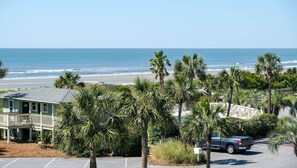 A beachfront property with a parking lot, a building with a balcony overlooking the ocean, and palm trees.