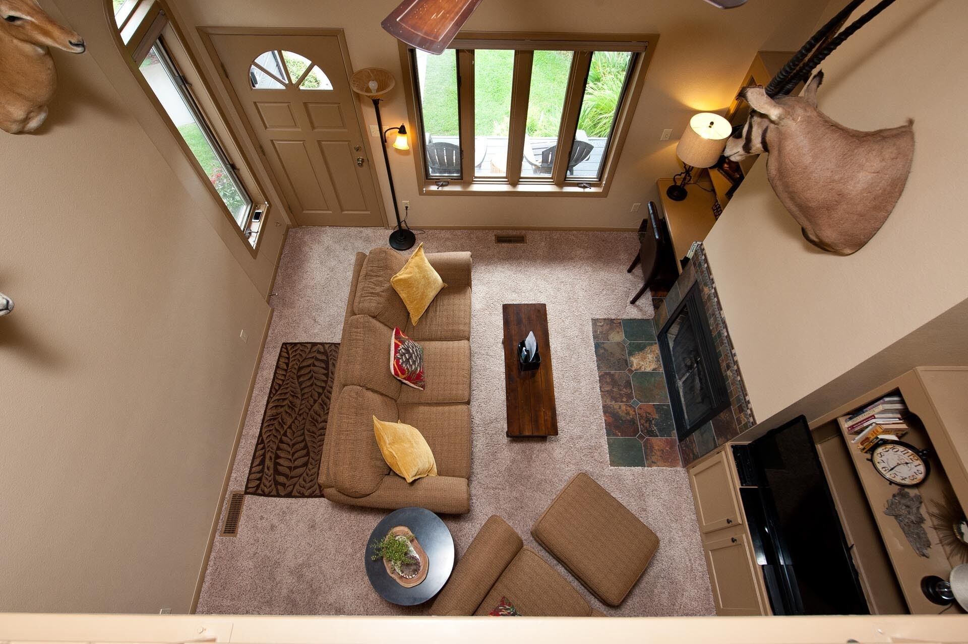 A spacious living room with a large sofa, a coffee table, and a fireplace. There are two windows providing natural light and a view of the outdoors.