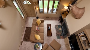 A spacious living room with a large sofa, a coffee table, and a fireplace. There are two windows providing natural light and a view of the outdoors. - Affordable Animas River Valley Townhome - A/C (Durango)