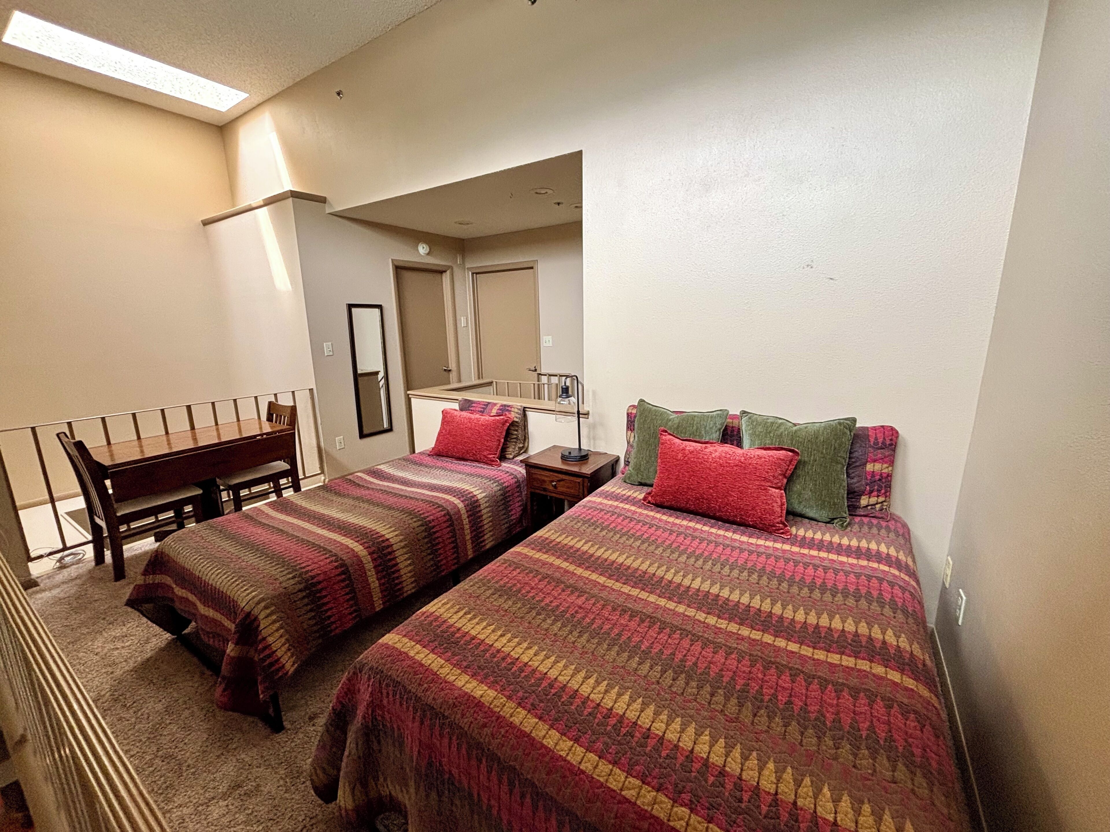 A compact bedroom with two beds, a desk, and a chair.
