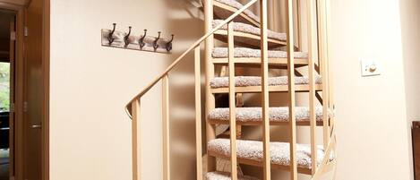 A spiral staircase with a wooden railing and carpeted steps, leading to an upper floor.