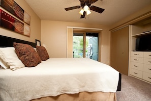 A bedroom with a bed, a ceiling fan, a TV, and a door leading to a balcony.