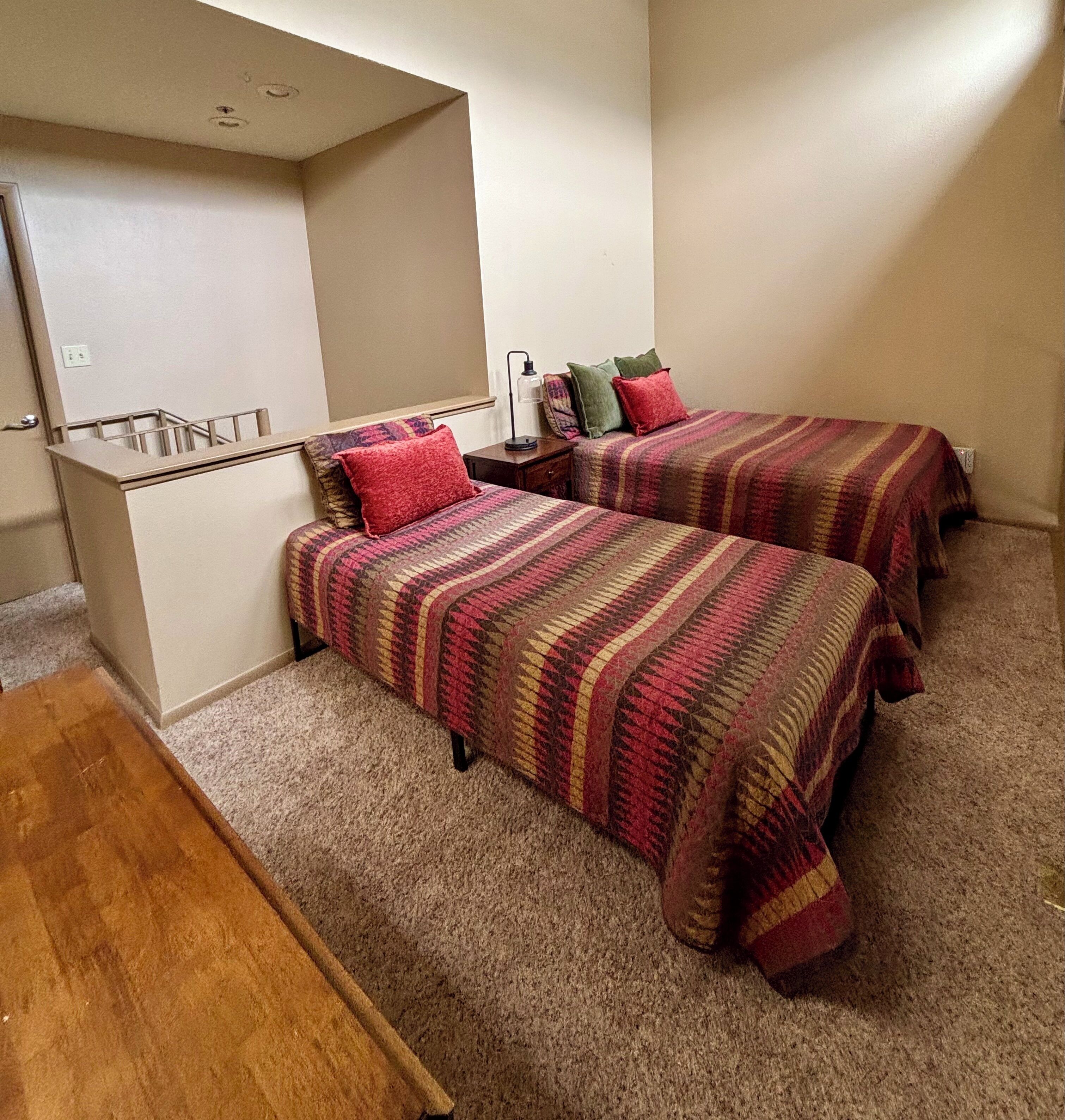 A bedroom with two beds, a desk, and a mirror.