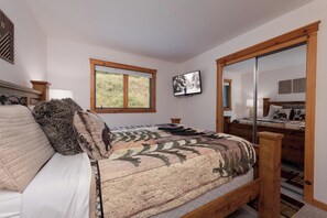 A bedroom with a large bed, a window, a television, and a mirror.