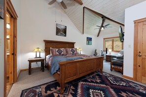 A bedroom with a wooden bed, two bedside lamps, a ceiling fan, a large window, and a door.