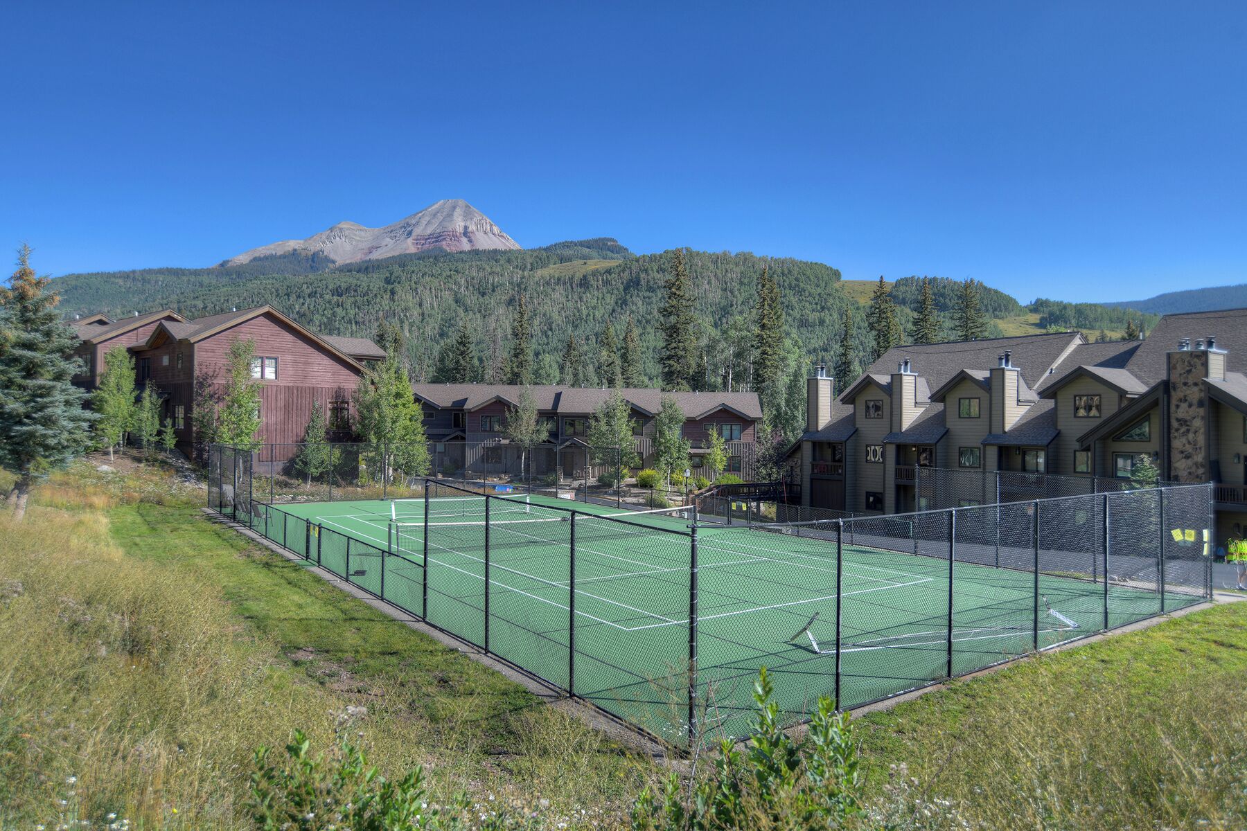 Ein Tennisplatz, umgeben von Chalets, mit einem Berg im Hintergrund.