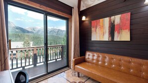 A room with a large sliding glass door leading to a balcony, a brown leather sofa, and a modern abstract painting on the wall.