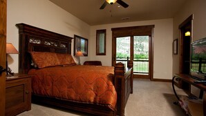 A bedroom with a large bed, wooden headboard, a ceiling fan, and a view through a glass door to an outdoor balcony.