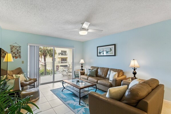A living room with a glass coffee table, two sofas, and a ceiling fan.