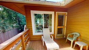 A wooden deck with a table and chairs, a wooden fence, and a window with a view of greenery.