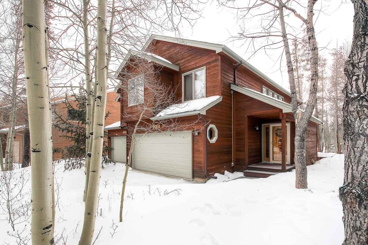 A wooden cabin with a garage, surrounded by trees and covered in snow.