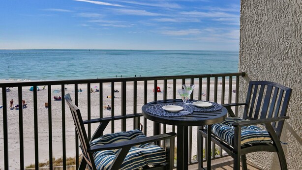 A balcony with a table and chairs overlooking a beach.