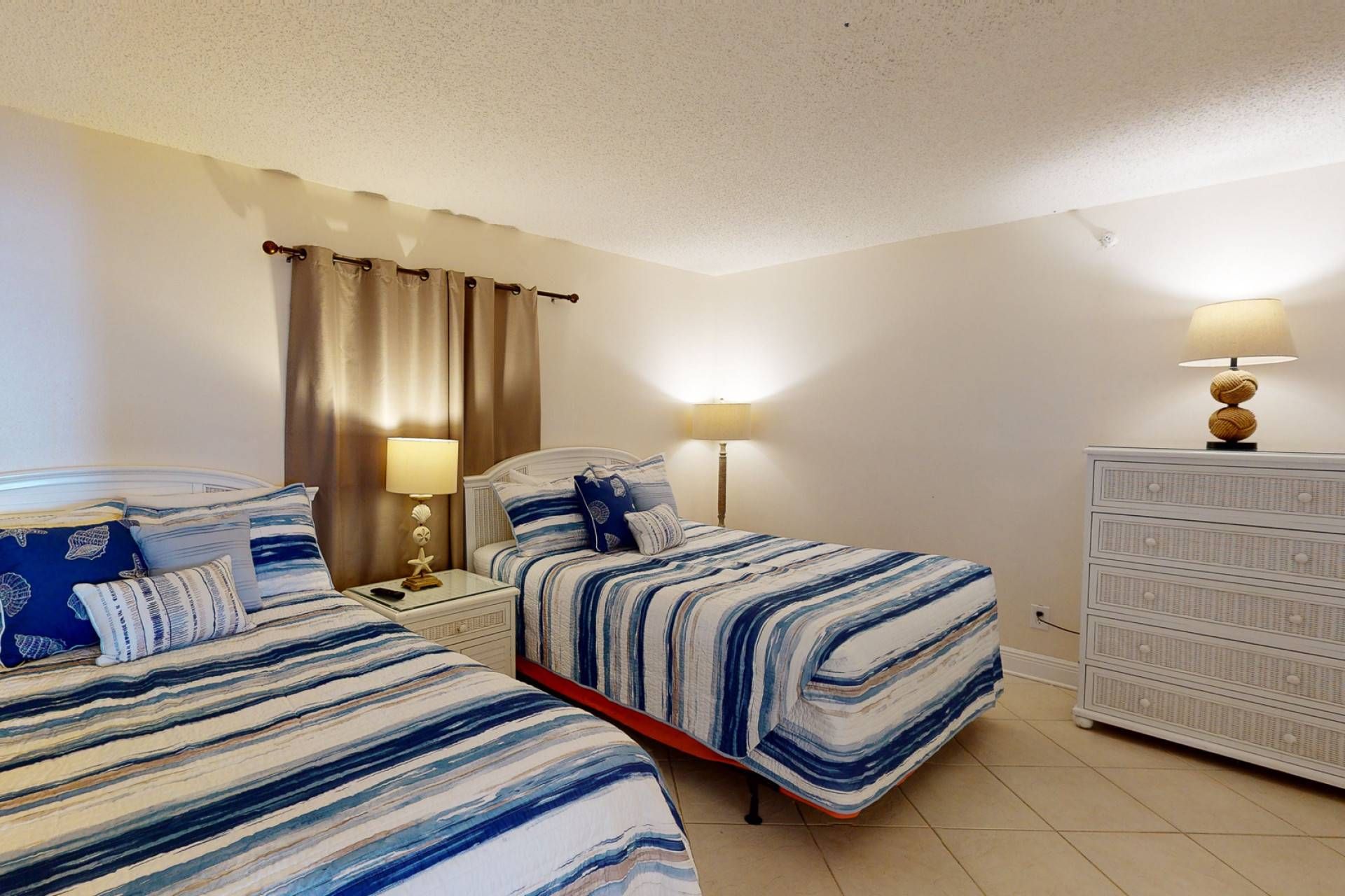 Habitación de hotel con dos camas, una mesita de noche con lámparas, un aparador y una cortina.