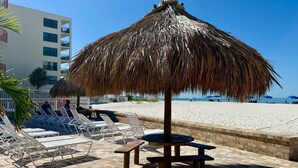 Zona de relax a la platja amb ombrelles de palla, gandules i una taula.