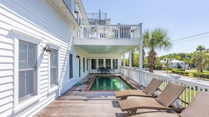 Un bâtiment blanc doté d’une terrasse en bois, d’une piscine et d’un balcon avec des chaises et une table.