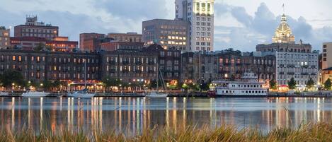 A waterfront cityscape with historic buildings, a river, and a boat docked near the shore.