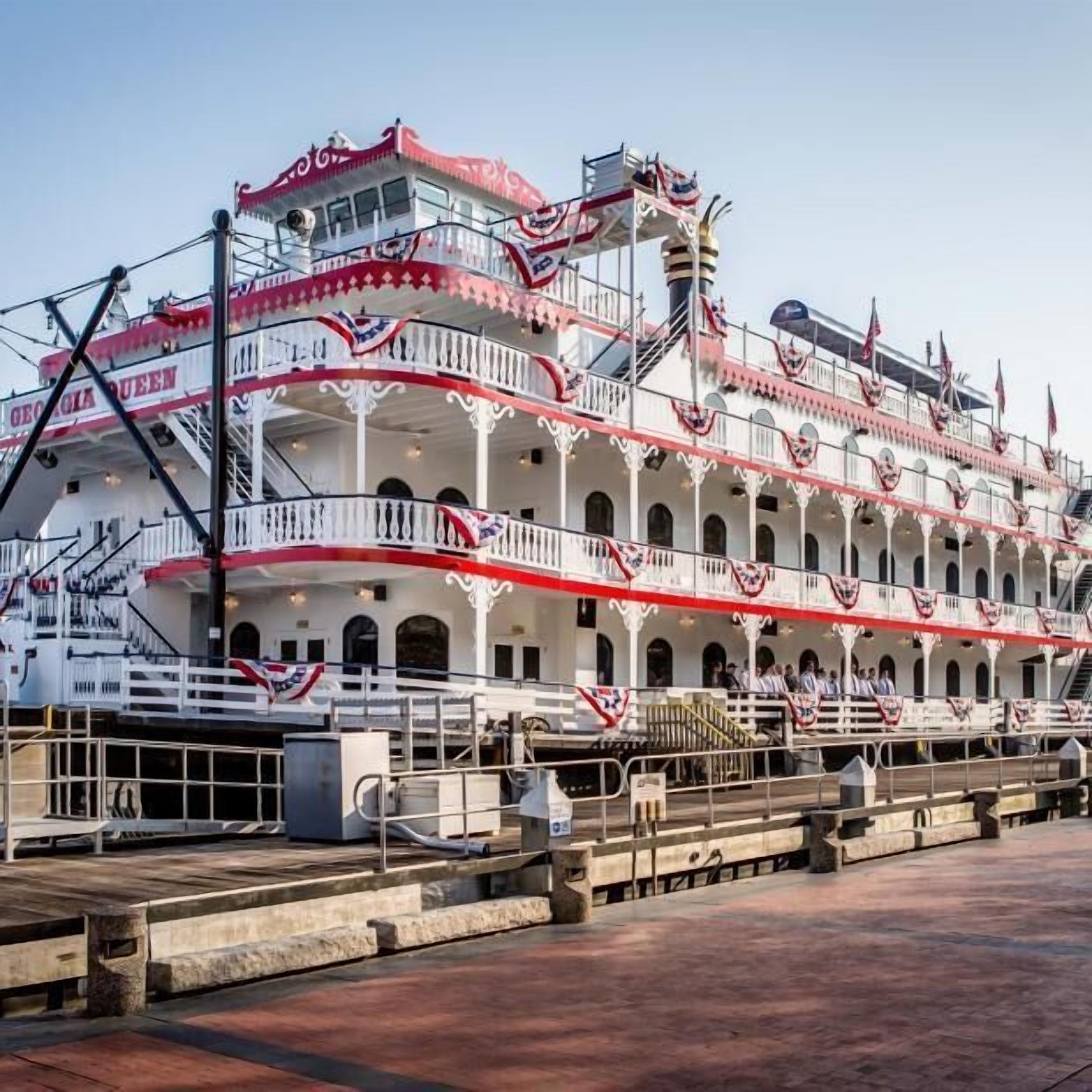 A large, multi-deck paddle steamer with balconies and railings, docked at a pier.