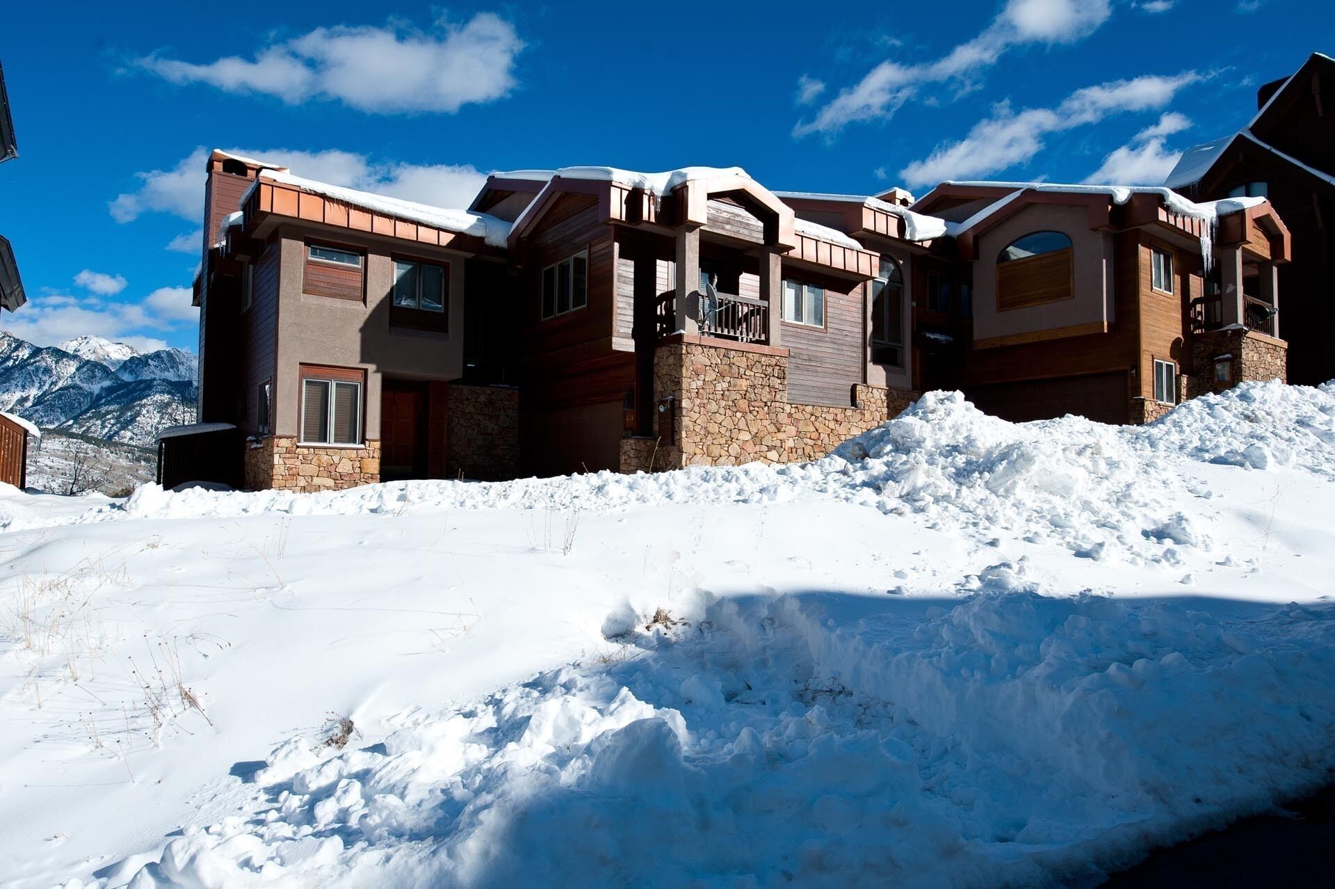 Un albergue de varias plantas con fachada de piedra y detalles de madera, rodeado de nieve y montañas.