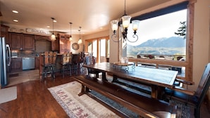A spacious kitchen with wooden cabinets, a dining area with a large wooden table and benches, and a view of mountains through a large window.