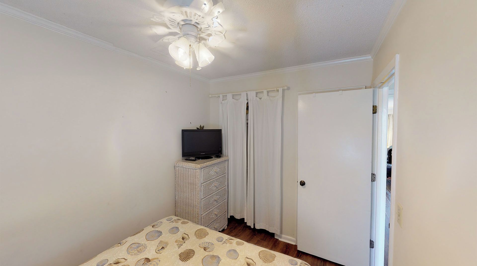 A bedroom with a bed, a dresser, a television, a ceiling fan, and a door.