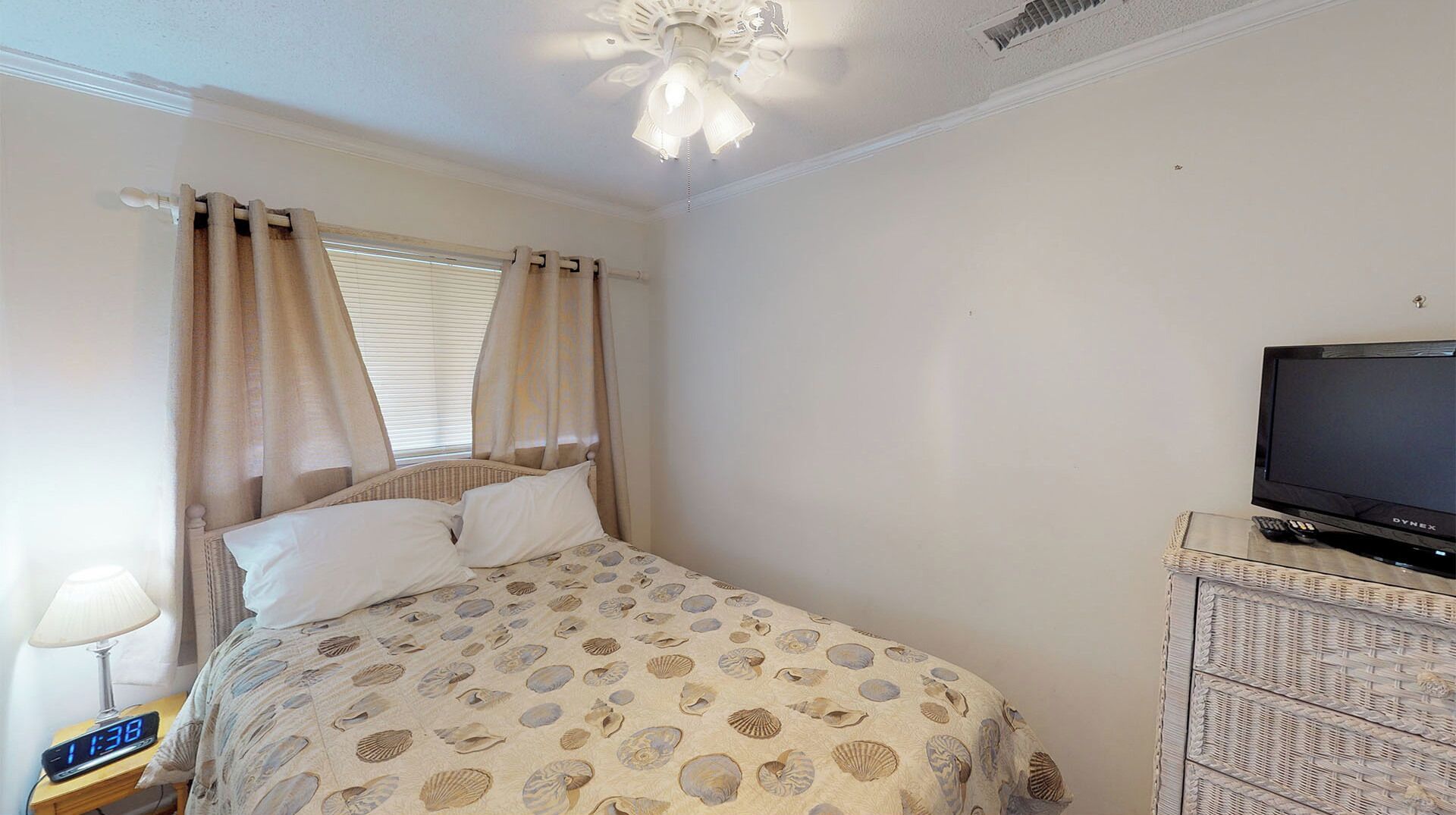 Een slaapkamer met een bed, gordijnen, een televisietoestel en een nachtkastje met een lamp.