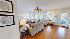 A spacious living room with a large sectional sofa, a ceiling fan, and a door leading to an outdoor area. - Updated home w/screened porch, golf view, walk to Marina/Dining and beach! (Isle of Palms)