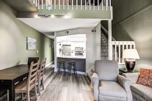Una cocina moderna con una isla central, un comedor con sillas de madera y una escalera que sube a un nivel superior.