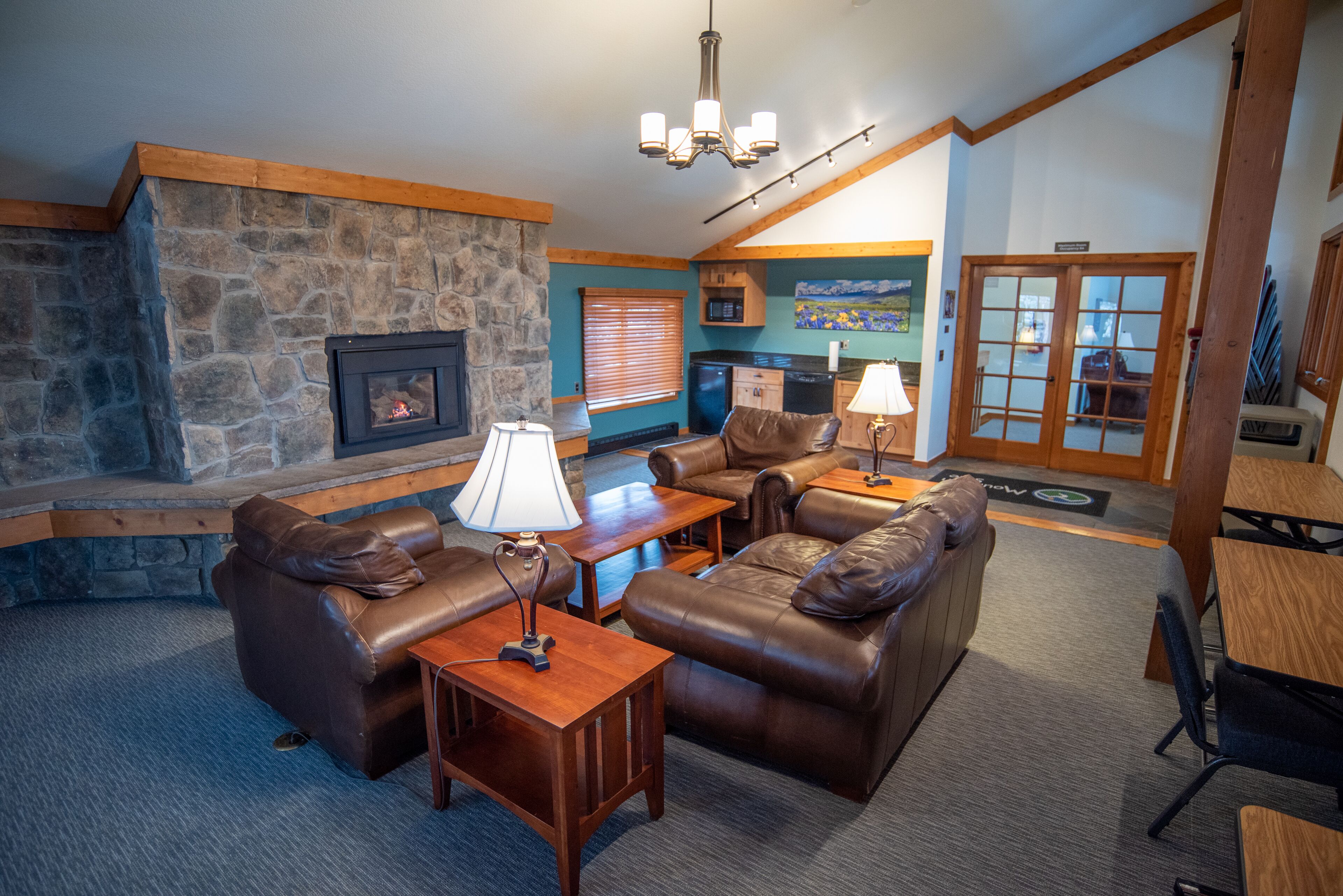 A cozy living room with leather sofas, a stone fireplace, wooden beams, and a dining area with a table and chairs.