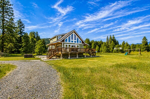 A two-story house with a deck, surrounded by a grassy yard and trees.