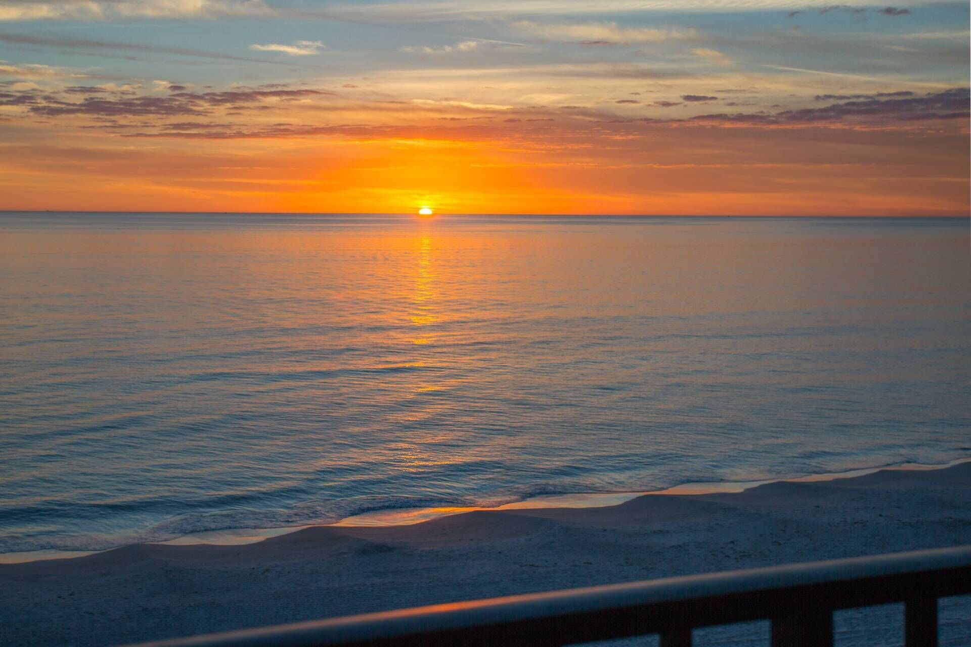 Een zonsondergang boven een rustige zee met een zandstrand op de voorgrond.