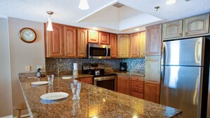 A modern kitchen with granite countertops, wooden cabinets, stainless steel appliances, and a clock on the wall. - Beachfront Condo With Private Balcony Overlooking the Sand! Relax on the Beach or Lounge in the Pool (Madeira Beach)