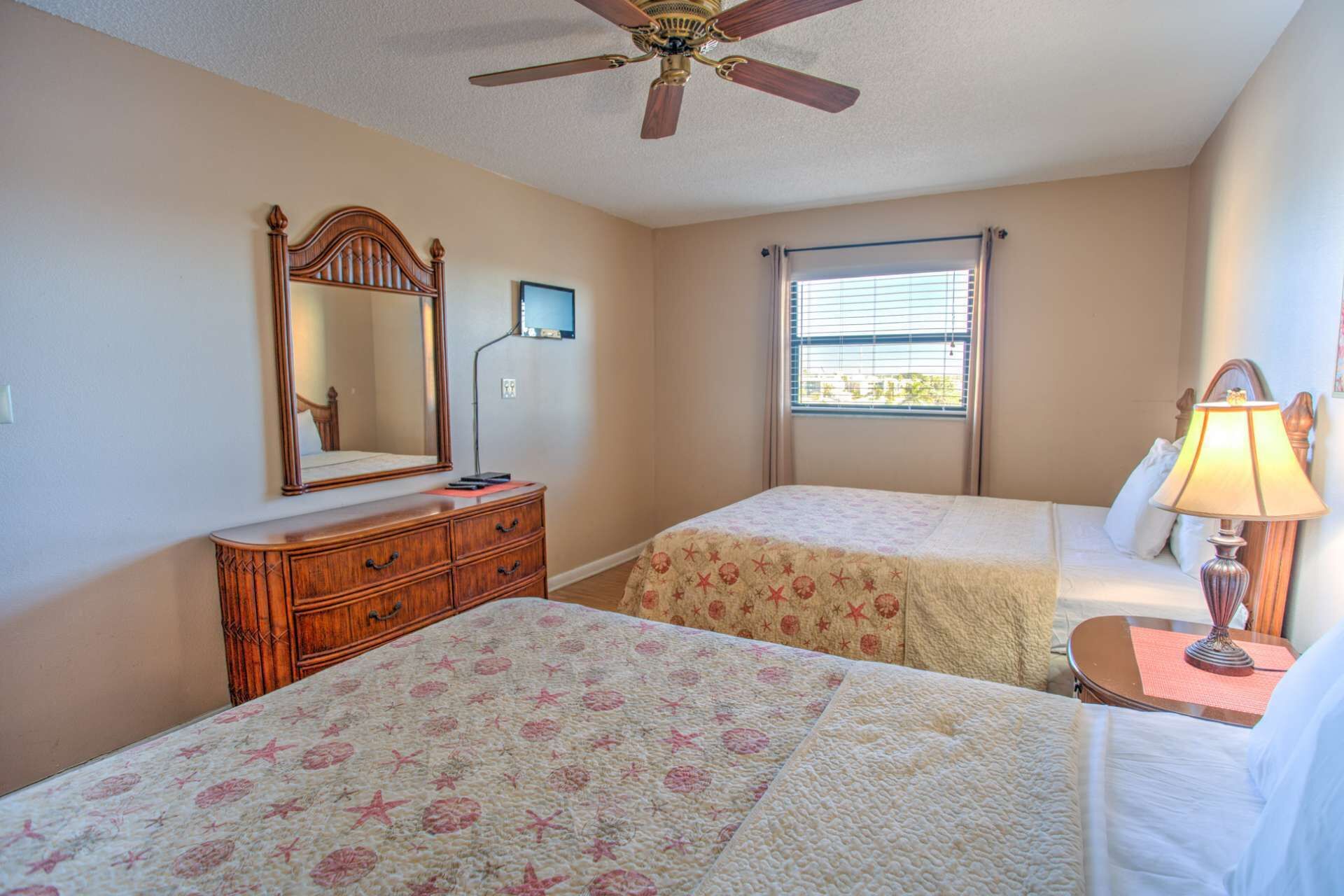 A bedroom with two beds, a dresser, a ceiling fan, a window with blinds, and a bedside lamp.