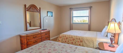 A bedroom with two beds, a dresser, a ceiling fan, a window with blinds, and a bedside lamp.