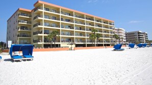 A multi-story hotel with balconies, a sandy beach in front, and blue lounge chairs. - Beachfront Condo With Private Balcony Overlooking the Sand! Relax on the Beach or Lounge in the Pool (Madeira Beach)