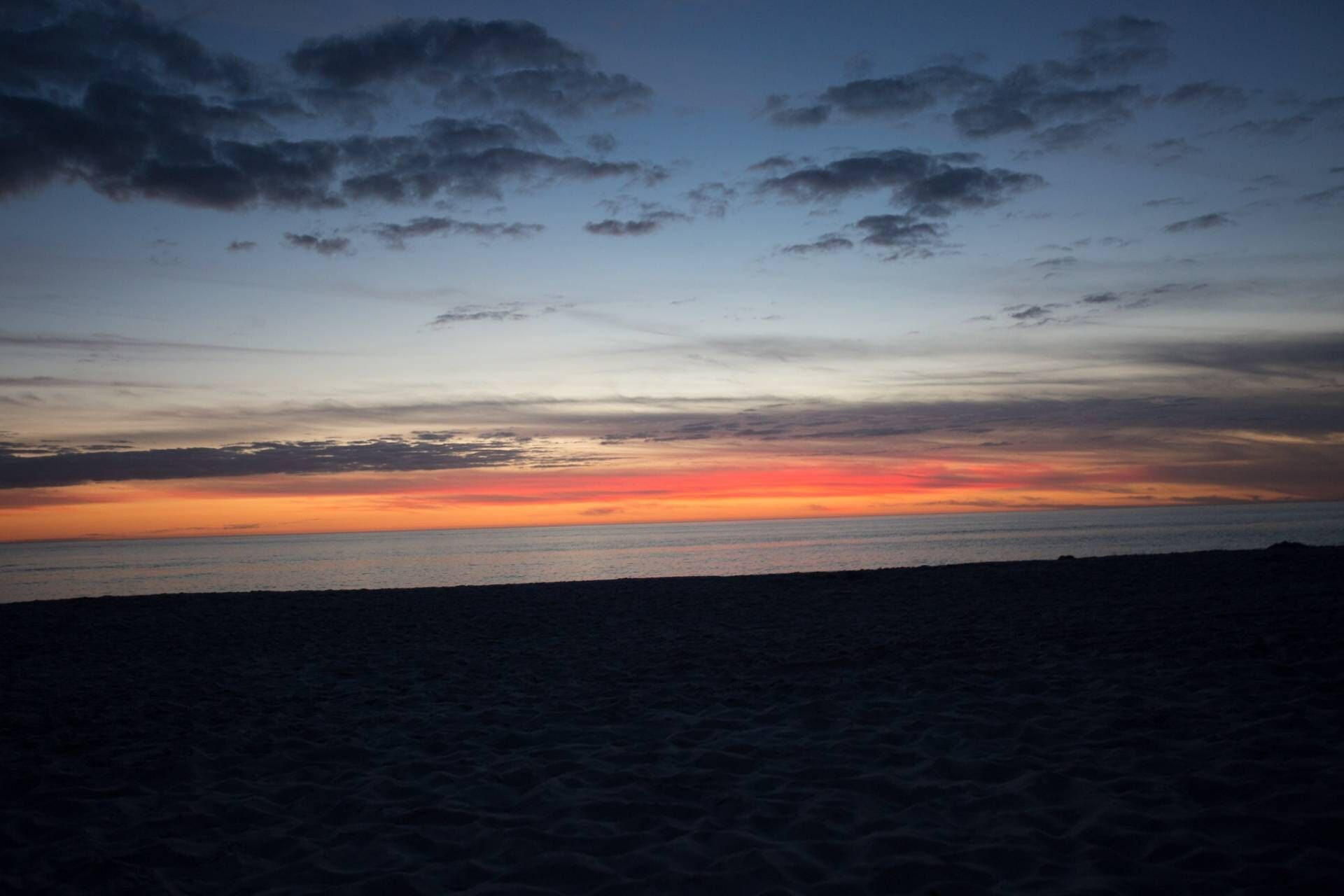 Ein Strand bei Sonnenuntergang mit klarem Himmel und ruhiger See.