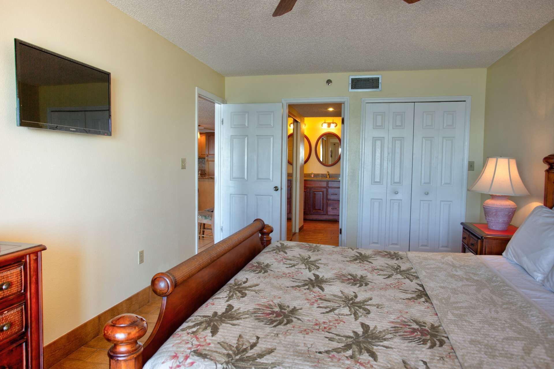 A bedroom with a bed, wooden headboard, a dresser, a nightstand, a lamp, and a ceiling fan.