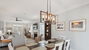 A dining area with a wooden table and white chairs, a chandelier, and framed pictures on the wall.