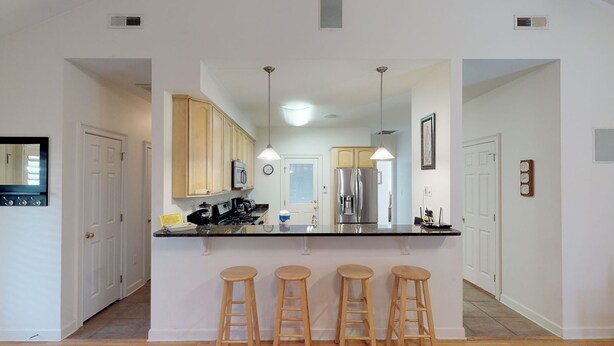 A modern kitchen with wooden cabinets, a stainless steel refrigerator, a coffee machine, and a bar stool area. - Spacious home just a short walk to the beach with a screen porch (Isle of Palms)