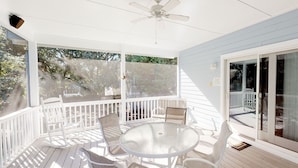 A covered outdoor area with a round table and chairs, a ceiling fan, and a view of the outdoors through large windows. - Spacious home just a short walk to the beach with a screen porch (Isle of Palms)