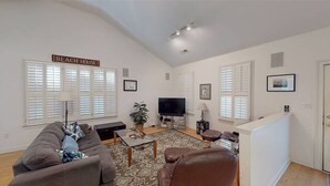A living room with a sofa, a coffee table, a TV, and a sign that reads "BEACH HOUSE". - Spacious home just a short walk to the beach with a screen porch (Isle of Palms)