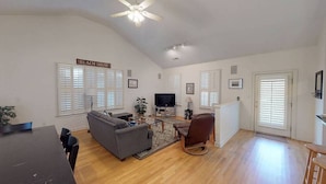 A spacious living room with a ceiling fan, a gray sofa, a brown armchair, a flat-screen TV, and a dining table with chairs. - Spacious home just a short walk to the beach with a screen porch (Isle of Palms)