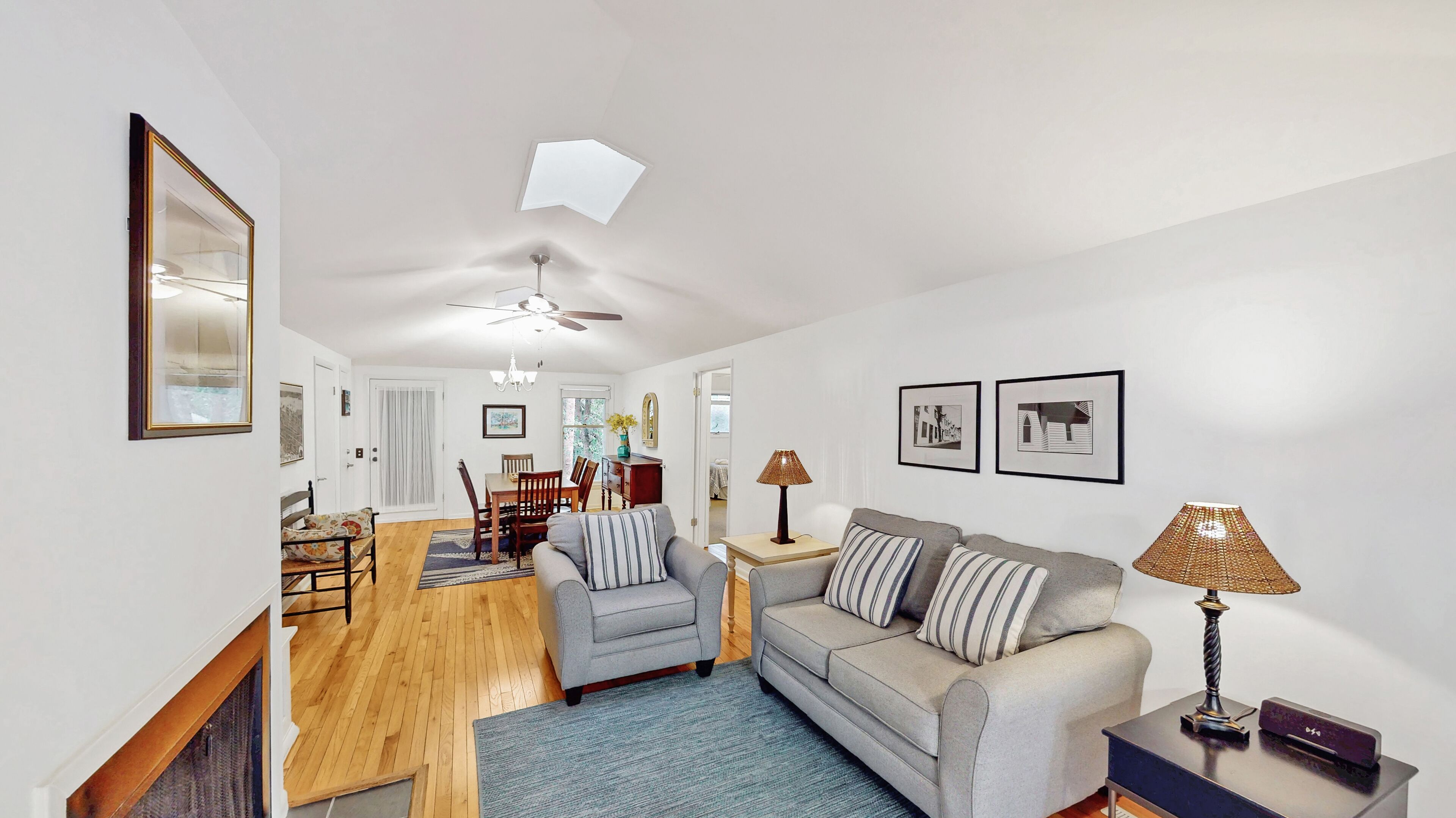 A living room with a sofa, a dining table, and chairs. There is a ceiling fan and a lamp on a side table.